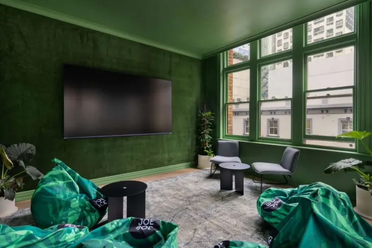 Salon aux murs verts avec grand écran et poufs au JO&JOE Auckland