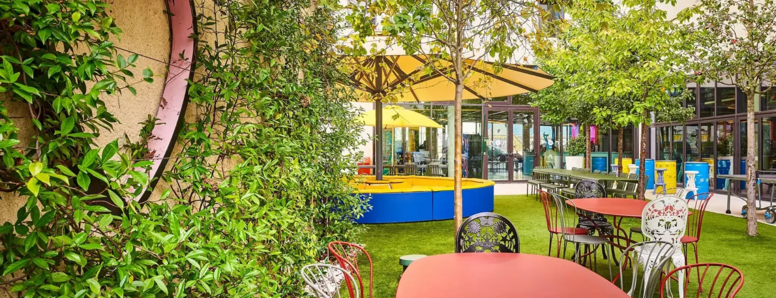 Terrasse jardin avec tables rouges, chaises et arbres au JO&JOE Paris Gentilly