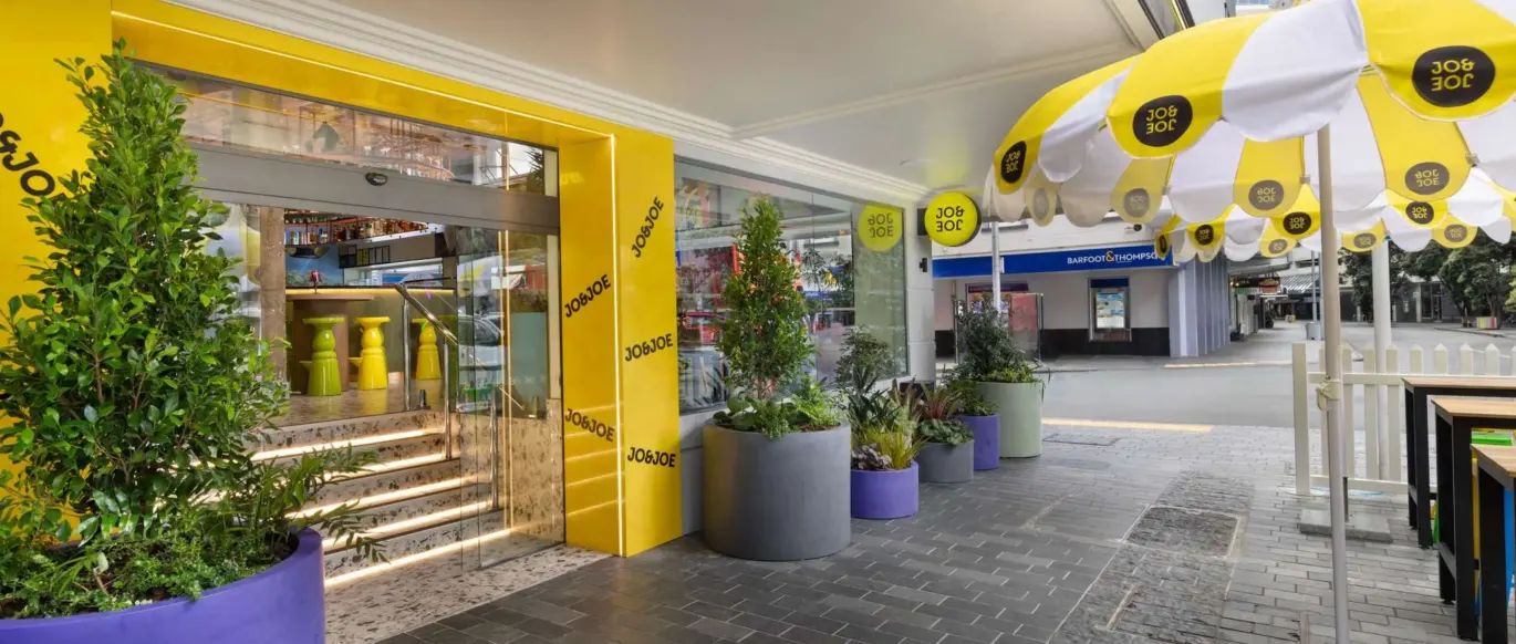 Entrée avec façade jaune et parasols au JO&JOE Auckland