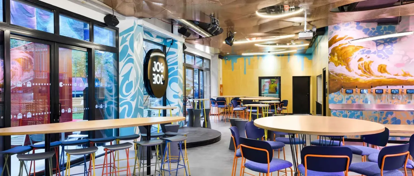 Espace commun avec tables hautes, tabourets et enseigne JO&JOE au JO&JOE Budapest