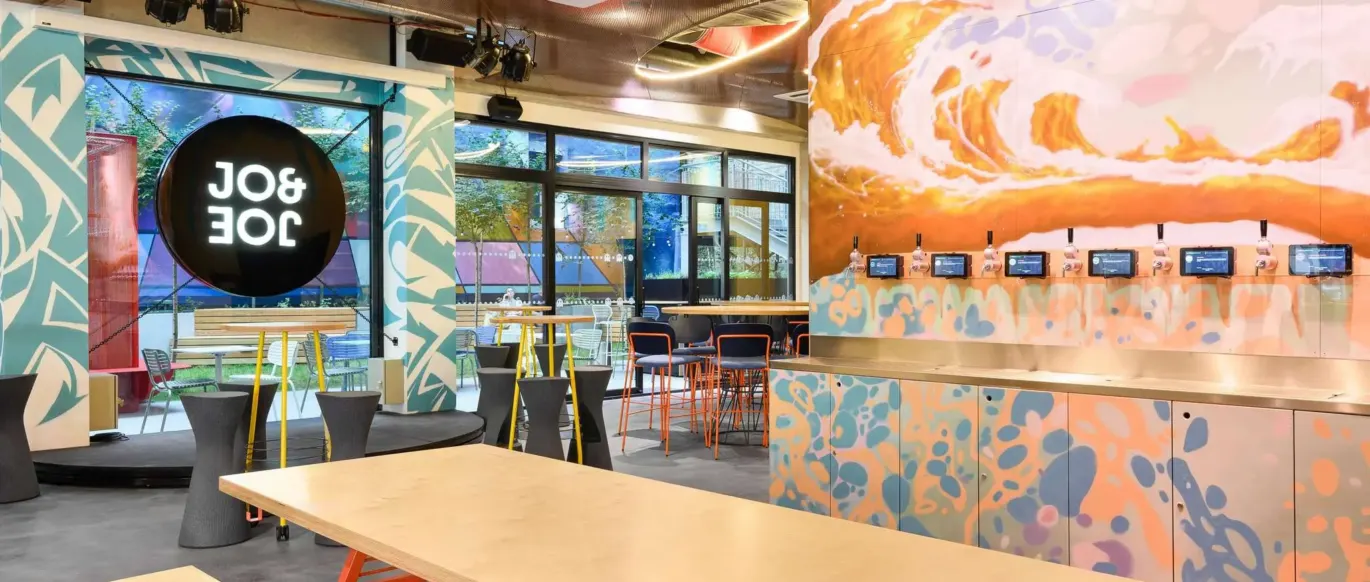 Espace commun avec table en bois, bancs et fresque murale au JO&JOE Budapest