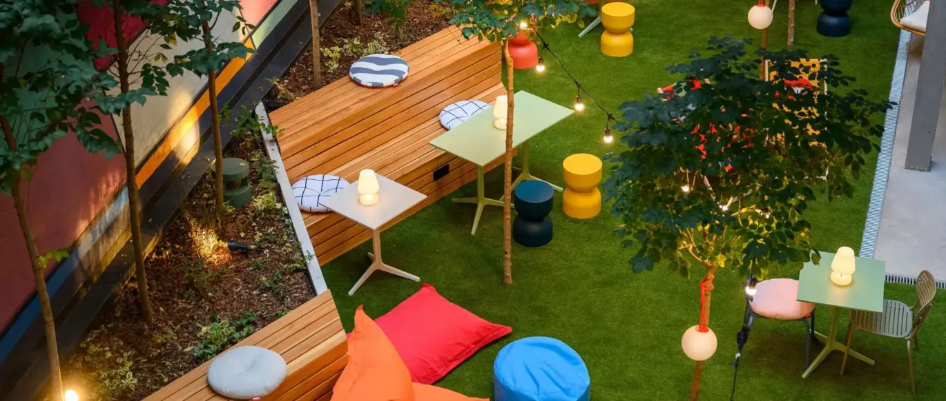 Terrasse jardin avec banquettes en bois, coussins et tables au JO&JOE Budapest