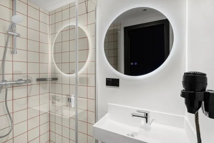 Salle de bains avec douche vitrée, miroir rond et lavabo au JO&JOE Budapest
