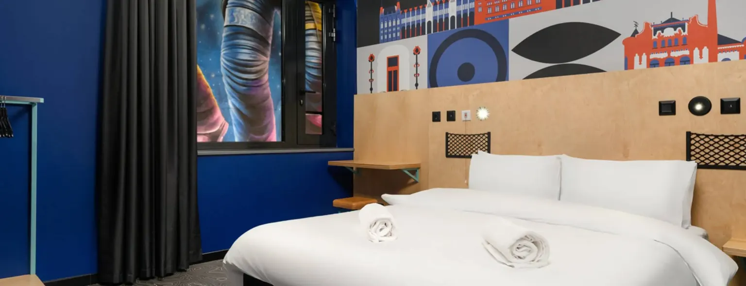 Lit double avec tête de lit en bois et mur illustré au JO&JOE Budapest