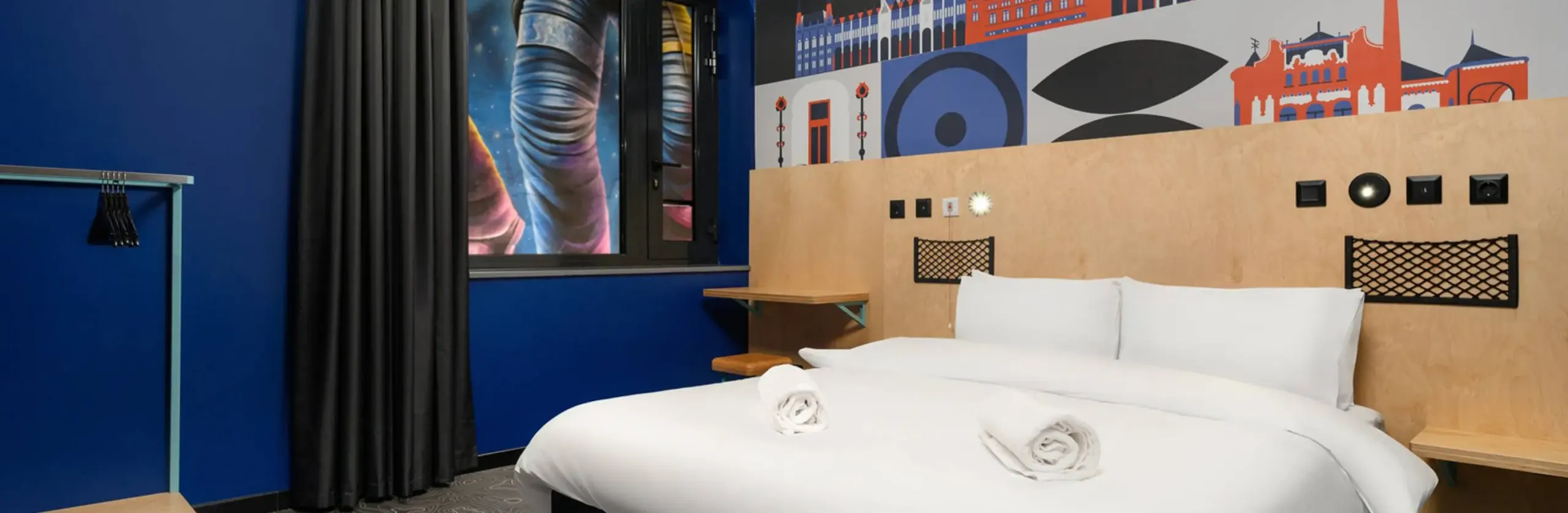 Double bed with a wooden headboard and an illustrated wall at JO&JOE Budapest