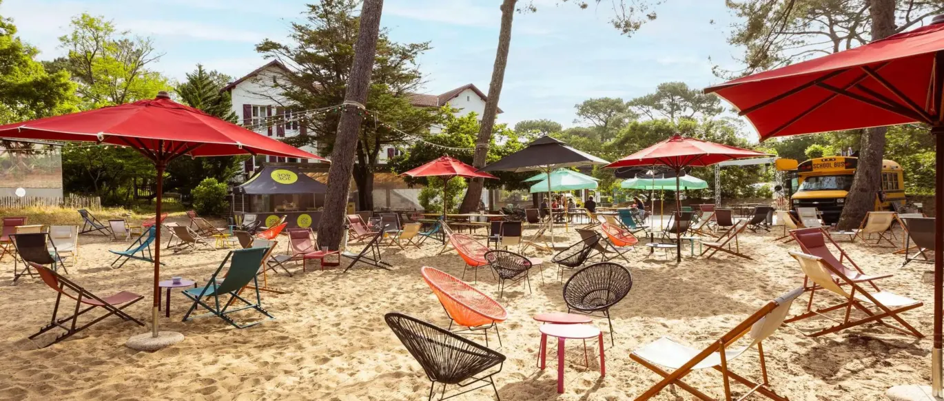 Espace extérieur sablonneux avec parasols et chaises au JO&JOE Hossegor