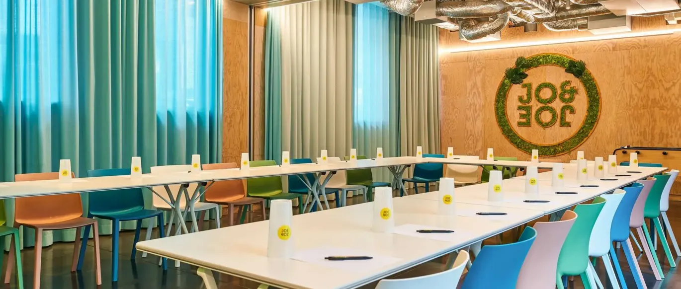 Salle de réunion avec longues tables et chaises colorées au JO&JOE Paris Gentilly