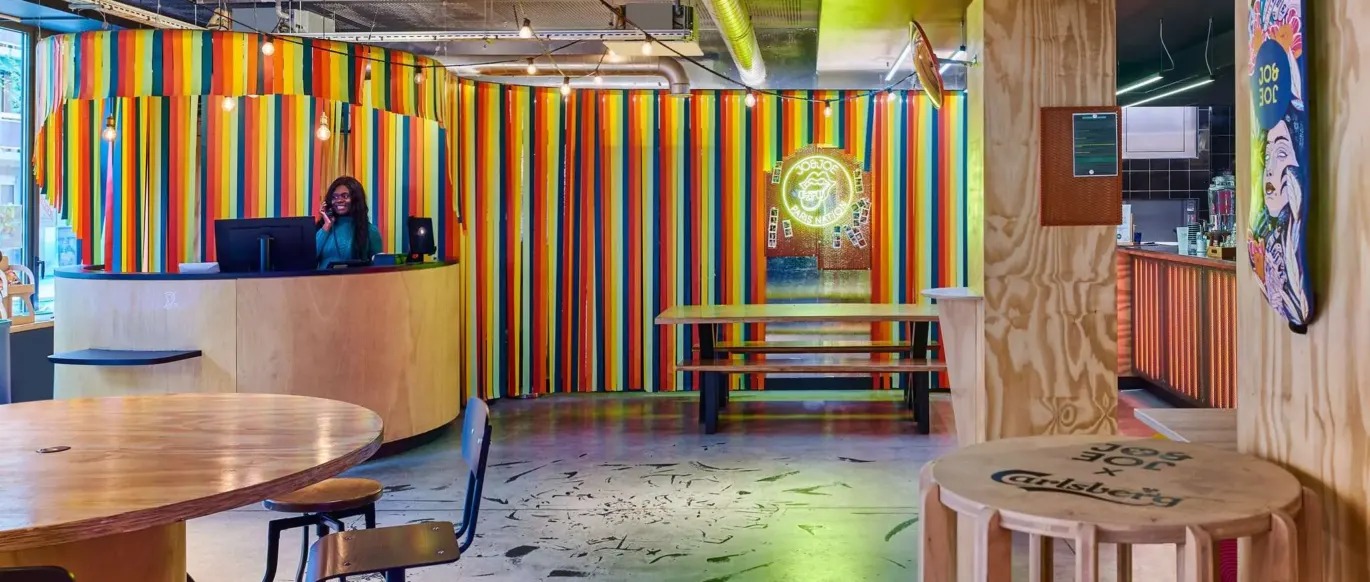 Réception avec mur à rayures colorées et comptoir en bois au JO&JOE Paris Nation