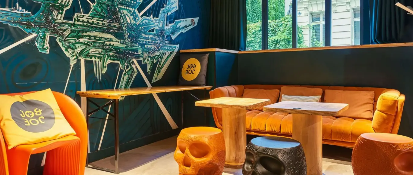 Salon avec canapé, tables et fresque murale au JO&JOE Paris Nation