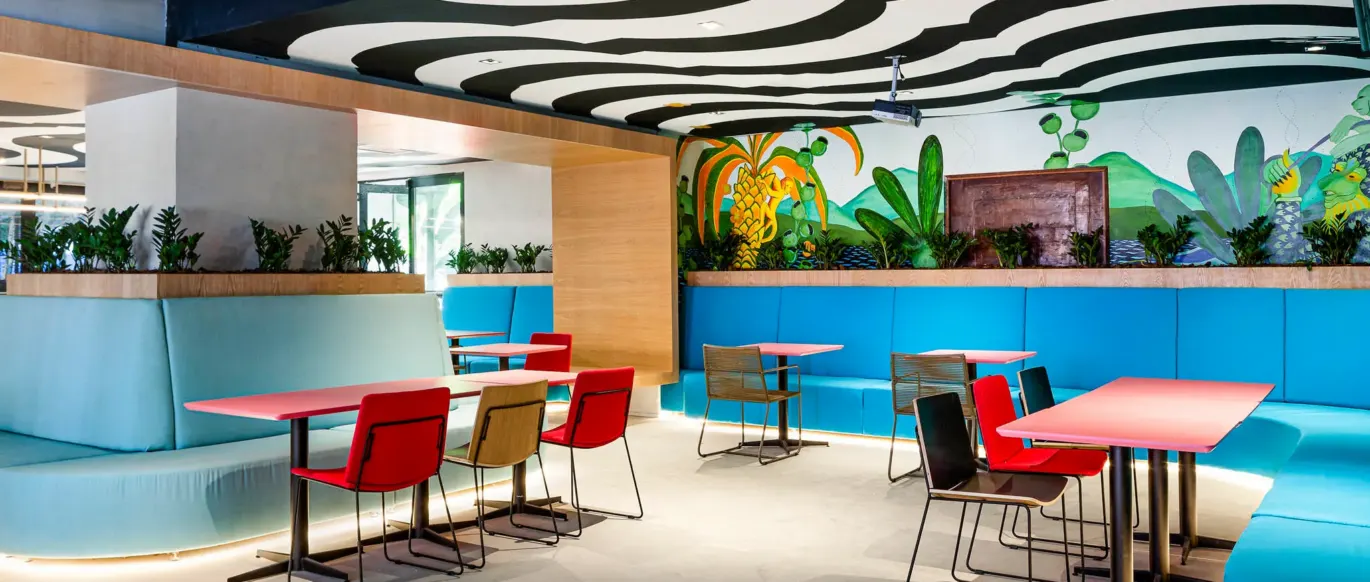 Espace commun avec banquettes bleues, chaises rouges et fresque tropicale au JO&JOE Rio de Janeiro