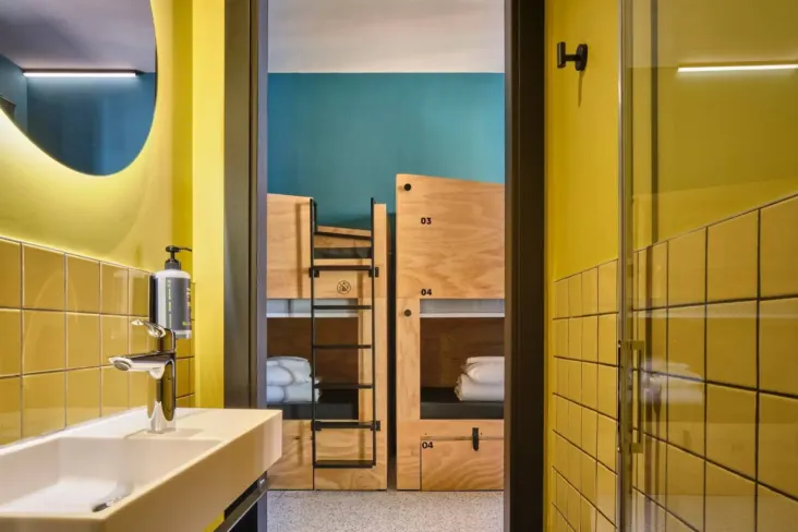 Dortoir avec lits superposés en bois vu depuis une salle de bains carrelée de jaune au JO&JOE Rome