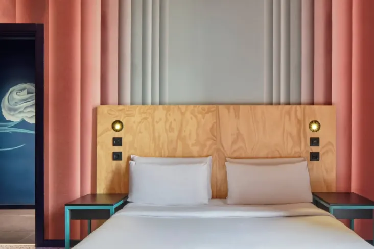 Lit double avec tête de lit en bois et rideaux roses au JO&JOE Rome