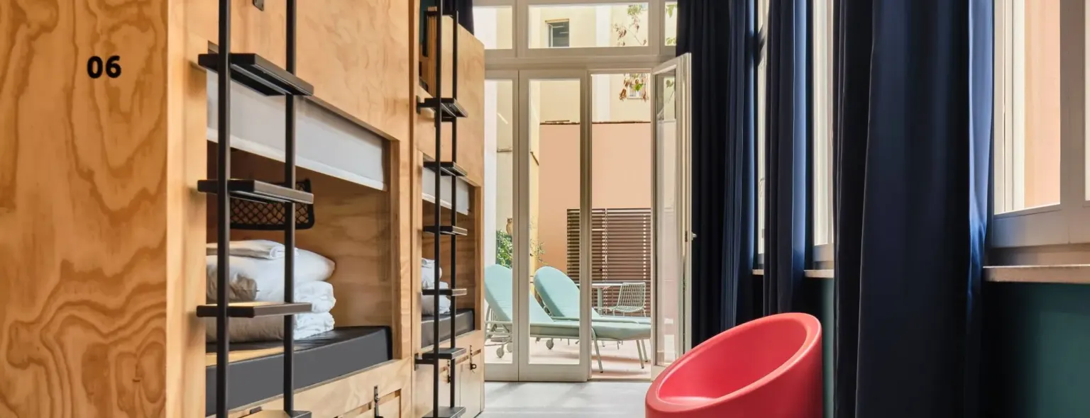 Lits superposés en bois dans un dortoir avec fauteuil rouge et accès à la terrasse au JO&JOE Rome